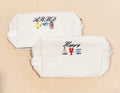 Two white pouches with embroidered designs and text on a beige background