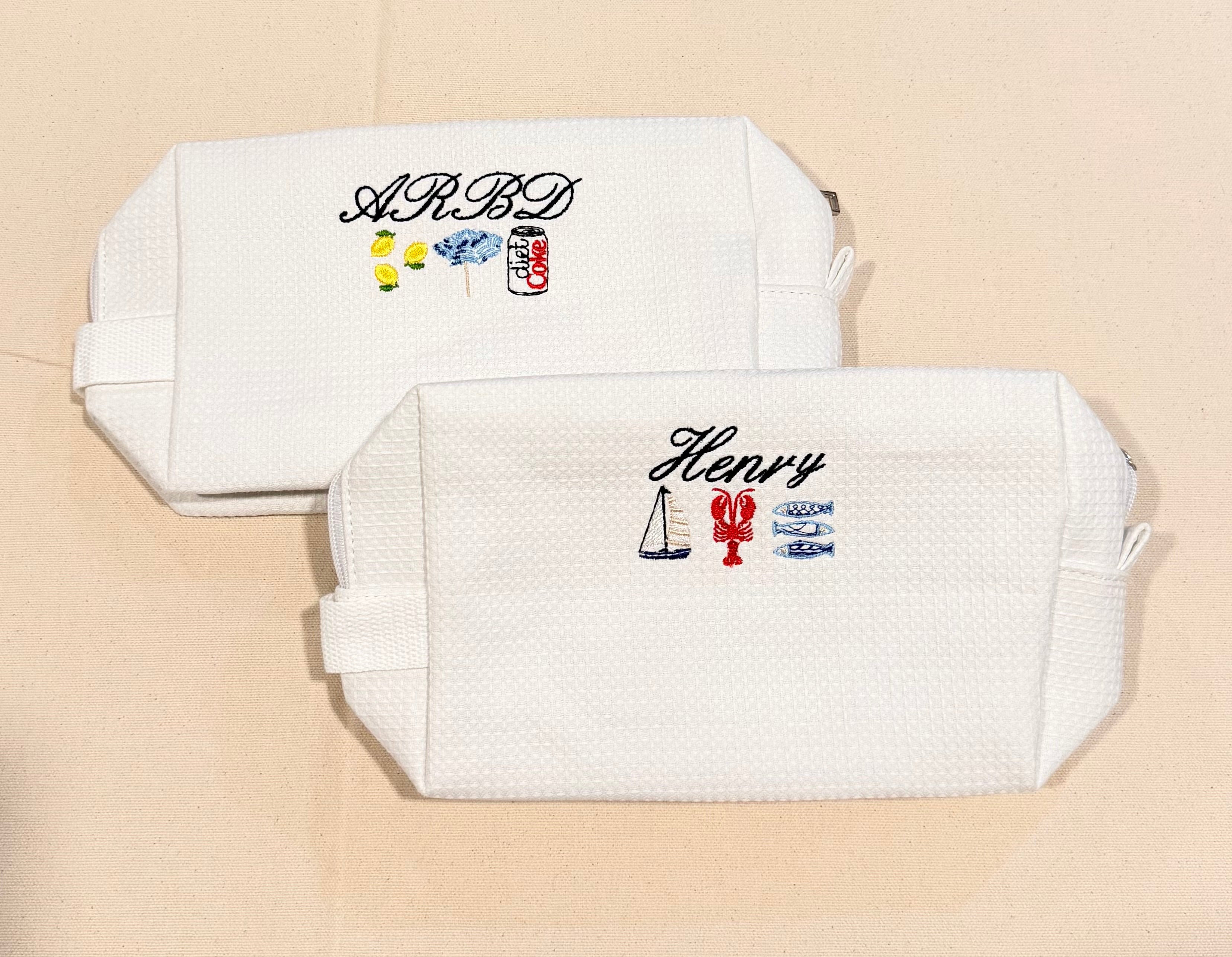 Two white pouches with embroidered designs and text on a beige background